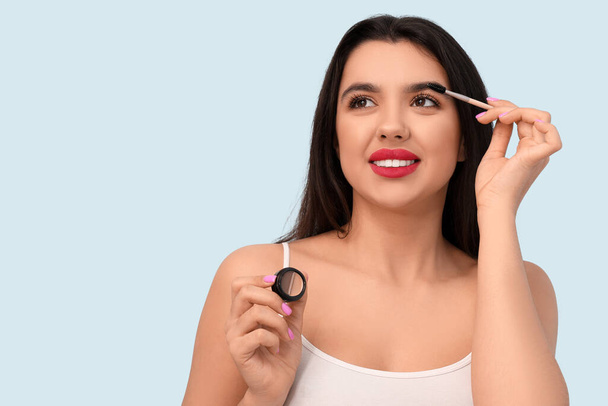 Beautiful young happy woman with makeup brush and brow gel on blue background - Фото, зображення