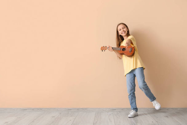 Nastolatka z ukulele wskazując na widza na beżowym tle - Zdjęcie, obraz