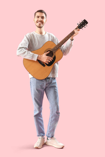 Handsome young man playing guitar on pink background - Foto, Bild