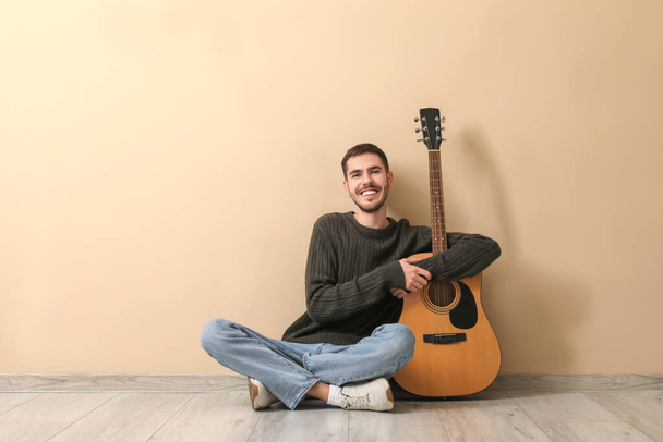 Hezký mladý muž s kytarou na béžovém pozadí - Fotografie, Obrázek