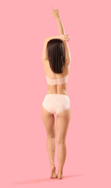 Mujer joven delgada en ropa interior de algodón sobre fondo rosa, vista trasera - Foto, imagen