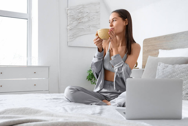 Sexy young woman with laptop drinking tea in bedroom - Photo, Image