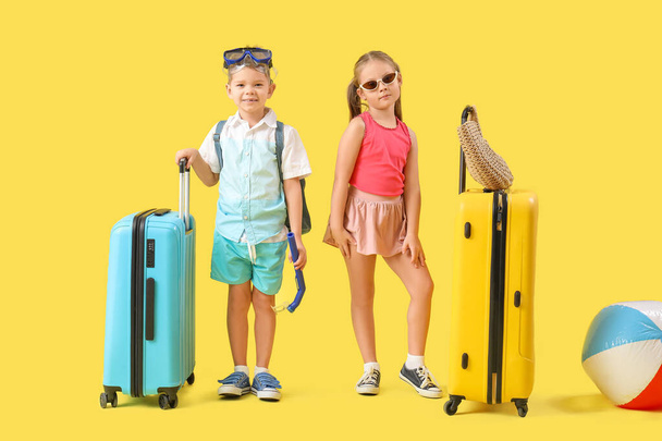 Χαριτωμένα μικρά παιδιά με βαλίτσες, ψάθινη τσάντα και μάσκα ψαροντούφεκου σε κίτρινο φόντο - Φωτογραφία, εικόνα