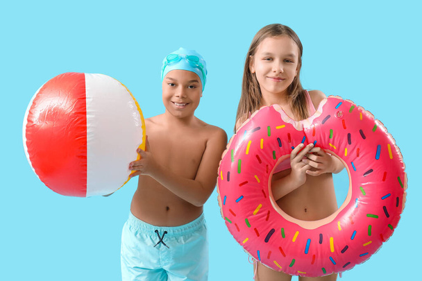 Cute little children in swimsuit with beach ball and inflatable ring on blue background - Photo, Image