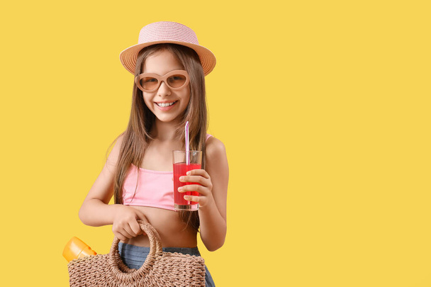 水着のかわいい少女, ウィッカーバッグと黄色の背景にジュースのガラスとサングラス - 写真・画像