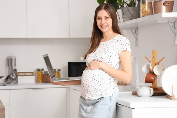Bella donna incinta con laptop in cucina - Foto, immagini