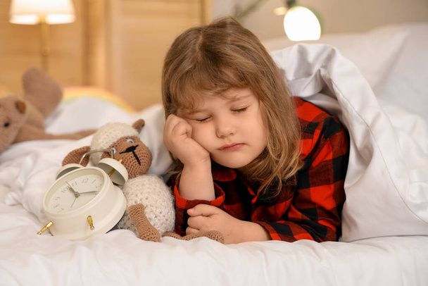 Suloinen pieni tyttö herätyskello ja pehmo lampaat nukkuvat sängyssä - Valokuva, kuva