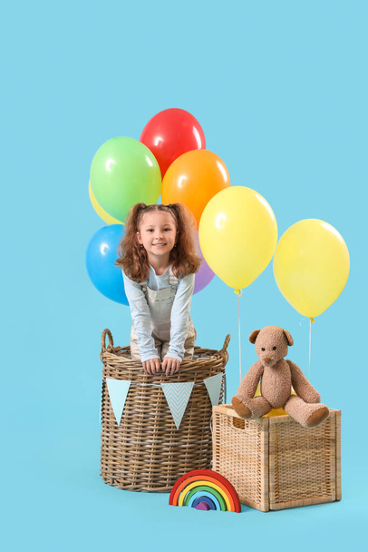 Sevimli küçük kız ve oyuncak ayı sepetlerde mavi arka planda balonlarla - Fotoğraf, Görsel