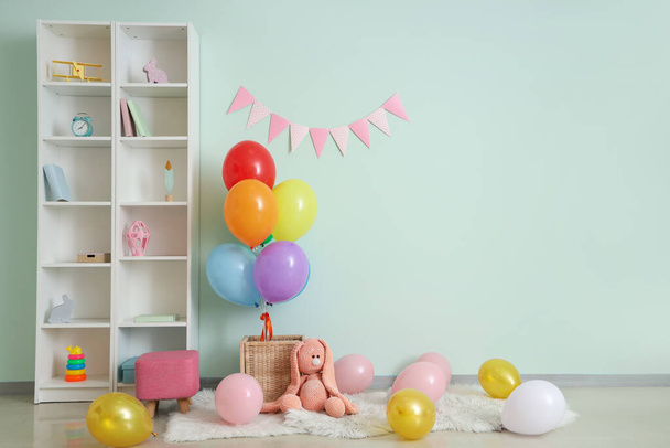 Kosz z balonami, króliczkiem zabawką i regałami przy jasnoniebieskiej ścianie - Zdjęcie, obraz