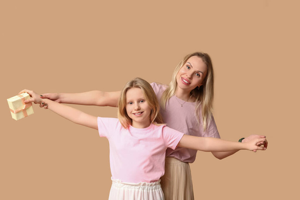 Schattig klein meisje met haar moeder en geschenkdoos voor moederdag op beige achtergrond - Foto, afbeelding