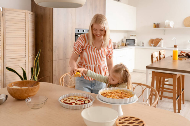 Happy mother with her little daughter squeezing lemon onto raw apple pie in kitchen - Photo, Image