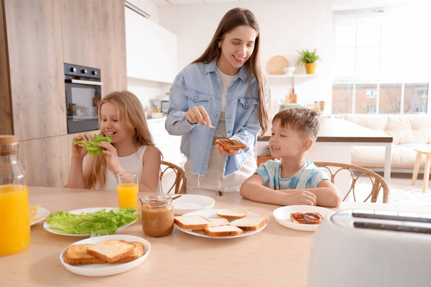 Kleine kinderen met hun moeder die toast maken aan tafel in de keuken - Foto, afbeelding