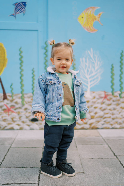 Petite fille souriante se tient près du mur peint coloré. Photo de haute qualité - Photo, image