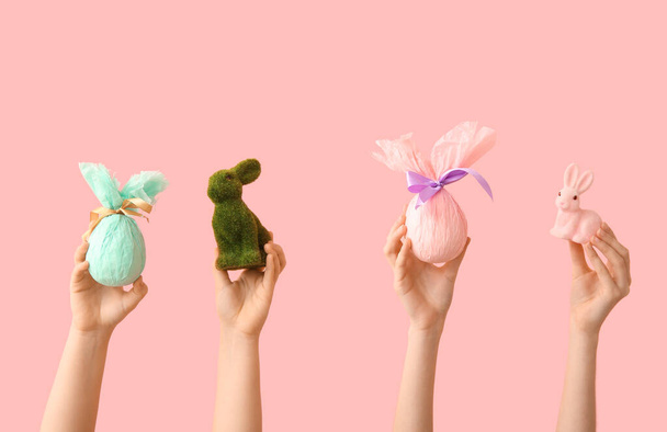 Manos femeninas con conejitos de Pascua y huevos de regalo sobre fondo rosa - Foto, Imagen