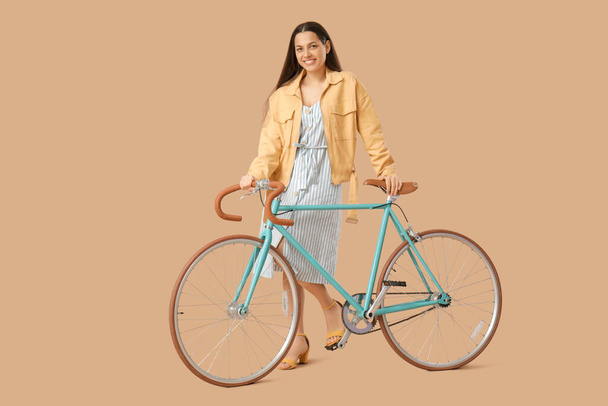 Schöne junge Frau mit Fahrrad auf braunem Hintergrund - Foto, Bild