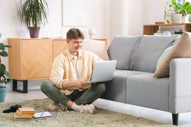 Männlicher Student mit Laptop lernt online auf dem Fußboden zu Hause - Foto, Bild