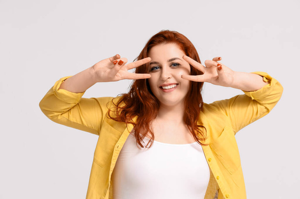 Smiling young redhead woman showing victory gesture on white background - Photo, Image