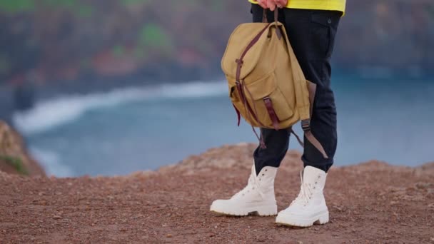 Ένα κορίτσι σε ένα τουριστικό ντύσιμο στέκεται στην άκρη ενός βουνού σε μπότες και με ένα σακίδιο, στην οποία το κύριο επίκεντρο της κάμερας κατευθύνεται. Σχέδιο ταξιδιού και περιπέτειας. - Πλάνα, βίντεο