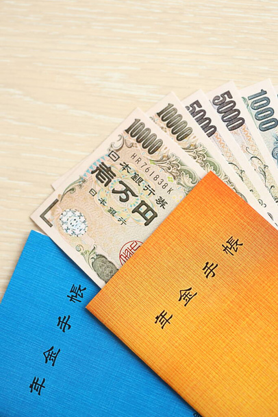 Japon emeklilik sigortası broşürleri yen para faturalarıyla dolu masada. Japon emekliler için mavi ve turuncu kitaplar kapanıyor. - Fotoğraf, Görsel
