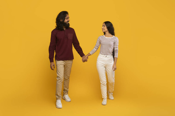 Két ember, egy férfi és egy nő, a mozgást szimbolizáló sárga háttérrel sétálnak és fogják egymás kezét. - Fotó, kép