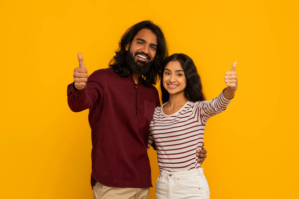 O casal alegremente endossa com polegares para cima e sorrisos radiantes, sugerindo positividade e alegria em um cenário amarelo - Foto, Imagem