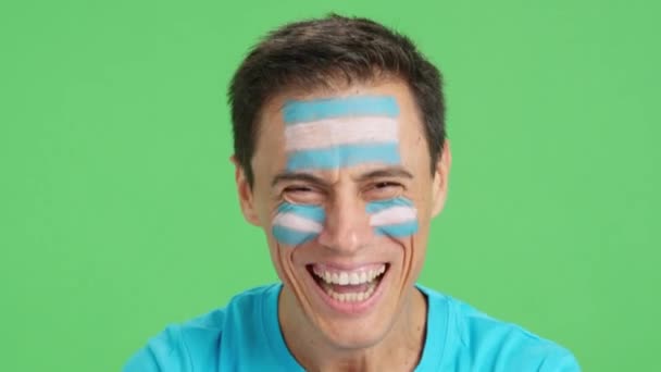 Wideo w studiu z chromą zbliżenia mężczyzny z argentyńską flagą namalowaną na twarzy uśmiechającego się do kamery - Materiał filmowy, wideo