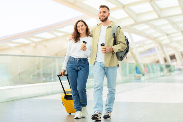 Pihentető fiatal pár alkalmi séta egy kortárs repülőtéren egy világos sárga bőrönddel - Fotó, kép