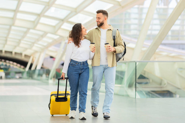 Молода пара посміхається і йде разом в сучасному аеропорту, передаючи відчуття подорожі і щастя - Фото, зображення