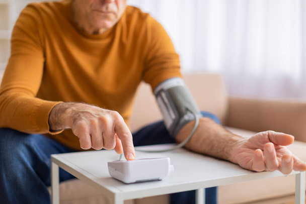 Ein reifer Mann überprüft seinen Blutdruck, veranschaulicht das Gesundheitsbewusstsein und die Bedeutung regelmäßiger Überwachung - Foto, Bild