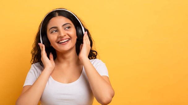 Uma jovem alegre com fones de ouvido desfruta de sua música favorita, ilustrando lazer e relaxamento - Foto, Imagem