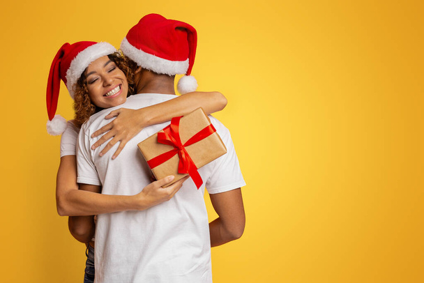 Weihnachtsgeschenk. glückliches schwarzes Mädchen umarmt ihren Freund für schönes Geschenk, orangefarbenen Hintergrund - Foto, Bild