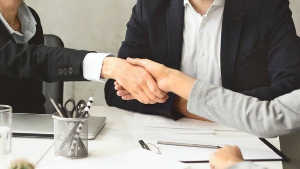 Dos profesionales que usan trajes estrechando las manos sobre un escritorio en una oficina, simbolizando acuerdo o trato - Foto, imagen