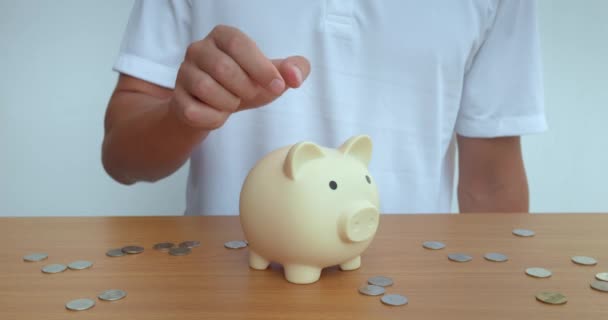 Man confidently puts coin into ceramic piggy bank, preserving savings. Person replenishes his untouchable savings. Coin falling into piggy bank for advertising banking services investments or savings - Footage, Video