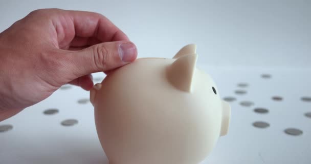 Hand throwing coin into piggy bank. Movement hand with coin towards piggy bank allows immerse yourself in process accumulating funds. Piggy bank is symbol financial security and ability to save - Footage, Video