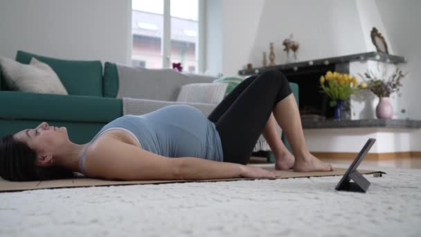 Вагітна жінка робить Йогу вдома у вітальні, майбутня мати піклується про тіло, щоб полегшити біль у спині під час третьої триместрової вагітності - Кадри, відео