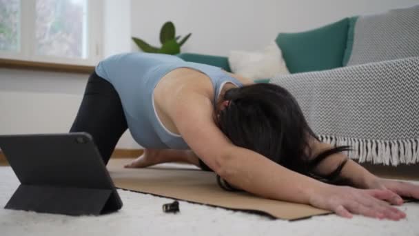 Беременная женщина растягивает тело во время занятий йогой на полу в гостиной. беременная мать заботится о спине перед настольным устройством - Кадры, видео