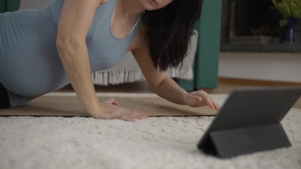 Femme enceinte sur le plancher du salon, s'engager avec une tablette pour choisir une application de conditionnement physique prénatal, axée sur la sélection de routine d'exercice sécuritaire à la maison - Séquence, vidéo