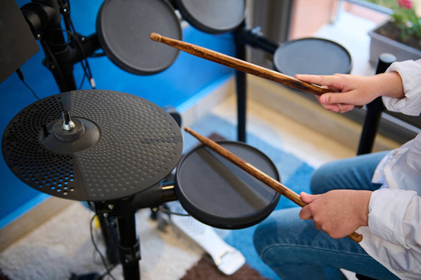 Γκρο πλαν άποψη από ψηλά των εφήβων χέρια ντράμερ. Ο έφηβος παίζει ντραμς στο στούντιο. Πάνω άποψη του αγοριού μουσικός ξυλοδαρμό στα μαύρα κύμβαλα με drumsticks, εκτέλεση ήχου που παίζει στο drum set - Φωτογραφία, εικόνα