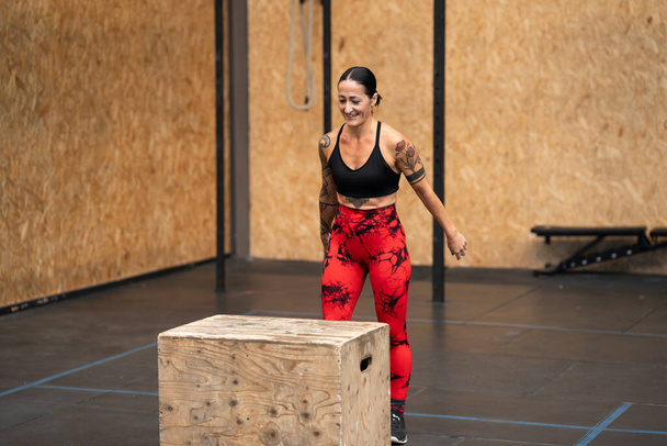 Glücklich starke erwachsene Frau im Begriff, in eine Box in einer Turnhalle zu springen - Foto, Bild