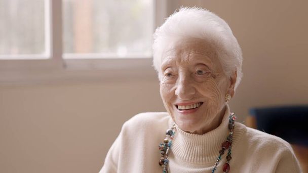 Mujer de edad con el pelo blanco sonriendo a la cámara en un geriátrico mirando al espacio de copia - Foto, Imagen