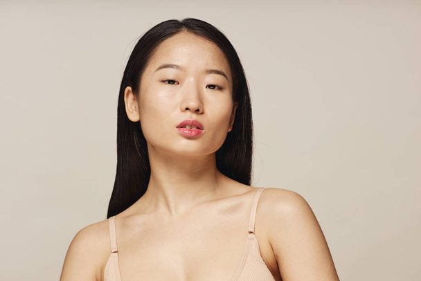 Retrato de estudio de primer plano mediano de mujer asiática joven con pelo largo con sujetador beige mirando a la cámara - Foto, imagen
