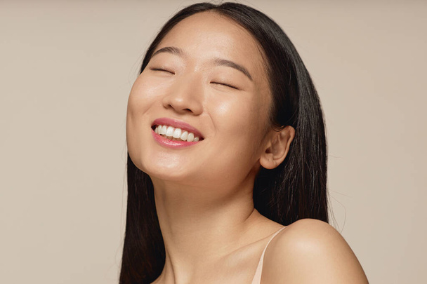 close-up studio portret van gelukkig jong aziatisch vrouw met lange rechte haar glimlachen met ogen dicht - Foto, afbeelding