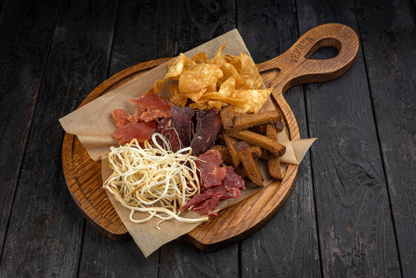 Variety of snacks on a wooden board on a dark wooden background - Foto, Imagem