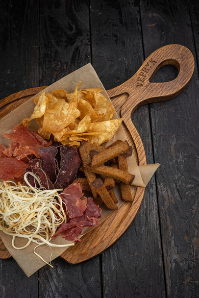 Variety of snacks on a wooden board on a dark wooden background - 写真・画像