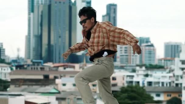 Ισπανόφωνος χορευτής break dancer πρακτική B-boy βήματα στην οροφή με την αστική θέα της πόλης ή ουρανό scrapper. Νεανικό μοντέρνο χορευτικό συγκρότημα που κάνει χιπ χοπ. Στυλ, μόδα, δράση. Υπαίθριο άθλημα 2024. hiphop. - Πλάνα, βίντεο