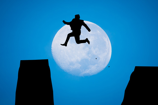 σιλουέτα άνθρωπος πηδώντας στην Ανατολή του ήλιου με μεγάλο φεγγάρι - Φωτογραφία, εικόνα