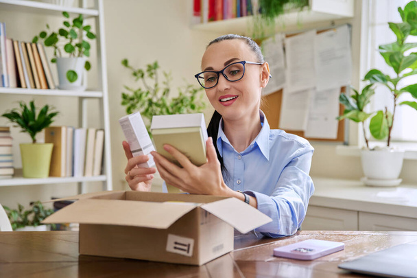 Satisfied female consumer buyer sitting at home unpacking cardboard box with online purchases. Happy woman unpacking boxes with cosmetics care products perfumes. Delivery by mail online store - Foto, Imagen