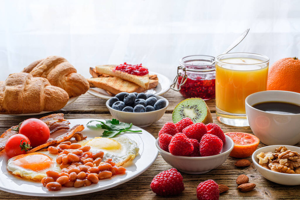 Πρωινό μπουφέ. Πλήρες αγγλικό και ευρωπαϊκό πρωινό. Μεγάλη ποικιλία από δεκατιανό φαγητό στο τραπέζι με αυγό, μπέικον, τοστ, χυμό πορτοκάλι, κρουασάν, καφέ, φρούτα και ξηρούς καρπούς. - Φωτογραφία, εικόνα