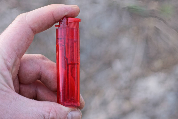 jeden starý červený plastový zapalovač leží na jeho ruce - Fotografie, Obrázek