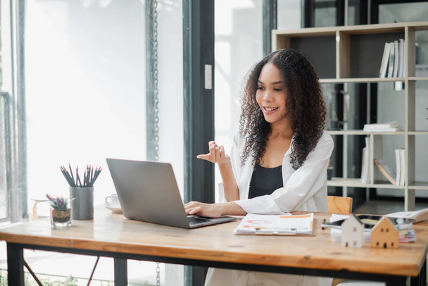 Geanimeerde jonge zakenvrouw die een levendig gesprek voert tijdens een virtuele bijeenkomst in een zonnige, moderne werkruimte. - Foto, afbeelding
